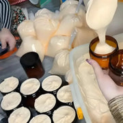 Production and packaging process of Zafrani face cream being poured into amber cosmetic jars from a large batch with bulk supply bags in the background.
